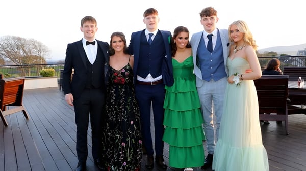 Eine Gruppe formell gekleideter Personen posiert auf einem Holzdeck mit landschaftlichem Hintergrund auf dem Gelände der Sligo Grammar School.