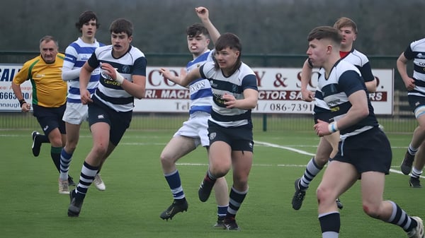 Schüler der Sligo Grammar School spielen ein intensives Rugby-Match auf einem Grasfeld mit Anzeigetafel im Hintergrund.