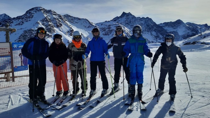 Eine Gruppe Schüler der Sligo Grammar School steht in Skibekleidung auf einer schneebedeckten Piste vor verschneiten Bergen.