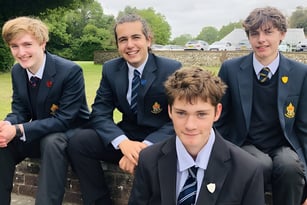 Vier männliche Schüler in Schuluniform sitzen auf einer Bank im Freien auf dem Campus des Slindon College.