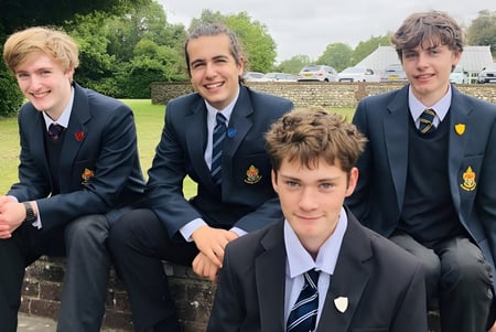 Vier männliche Schüler in Schuluniform sitzen auf einer Bank im Freien auf dem Campus des Slindon College.