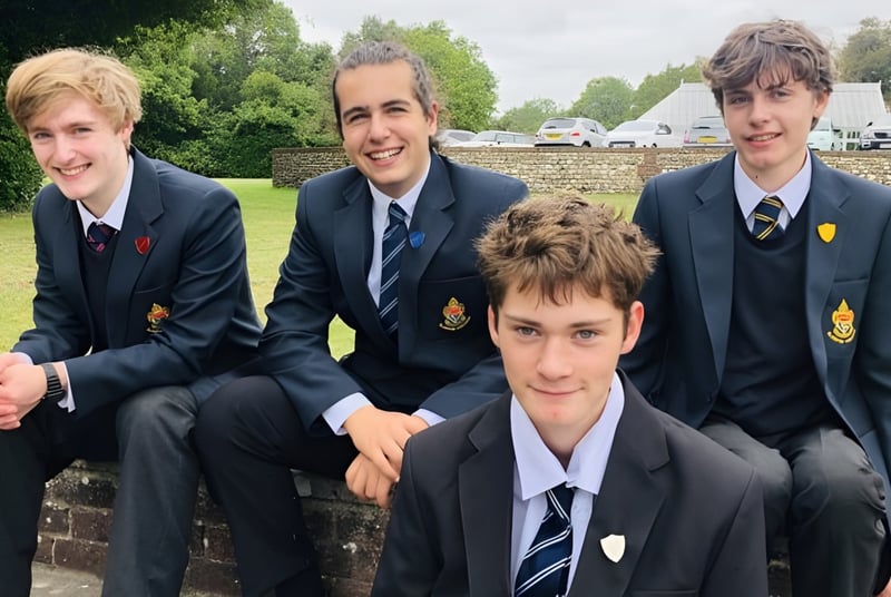 Vier Schüler in Schuluniform sitzen zusammen auf einer Bank im Freien auf dem Campus des Slindon College.