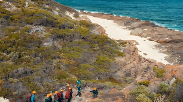 Eine Gruppe Schüler wandert auf einem Küstentrail mit Blick auf einen türkisfarbenen Ozean und einen Sandstrand bei der Smithfield State High School.