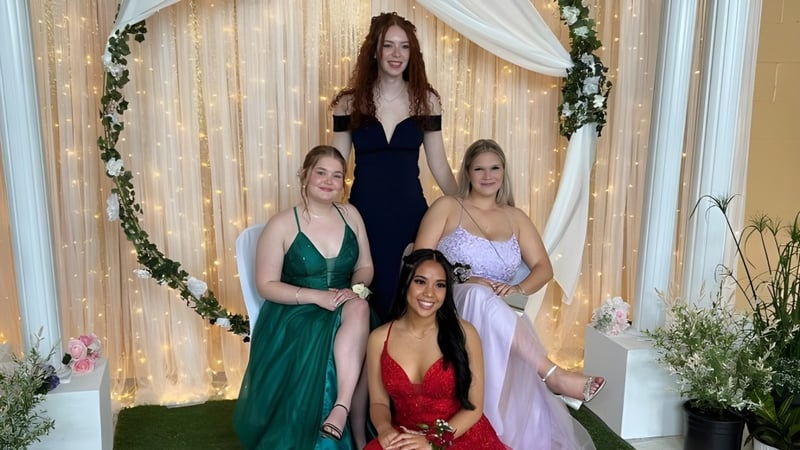 Vier junge Frauen in formeller Kleidung posieren zusammen vor dekorativem Hintergrund auf dem Campus des Smiths Falls District Collegiate Institute.