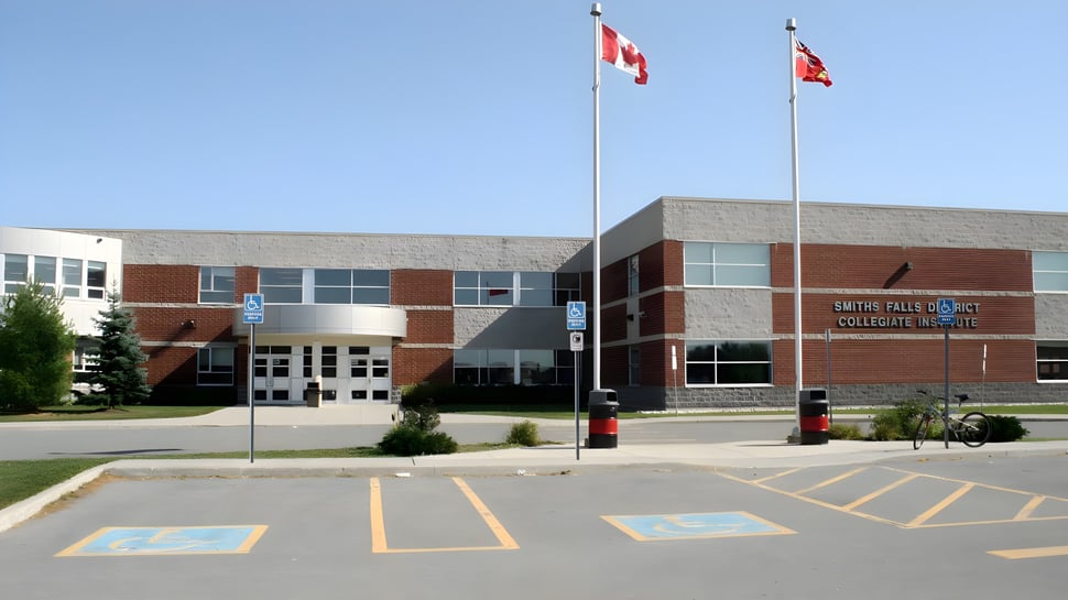 Das moderne mehrstöckige Gebäude mit kanadischen Flaggen der Smiths Falls District Collegiate Institute ist von einem Parkplatz mit Behindertenparkplätzen umgeben.