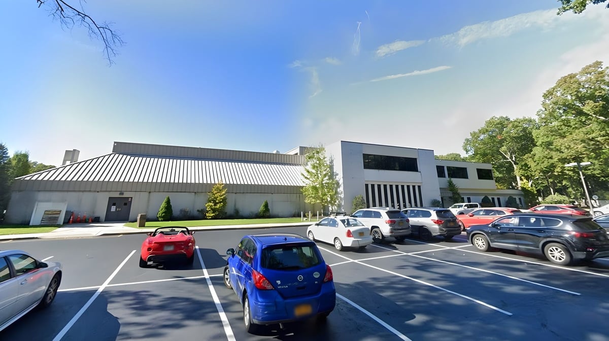 Das moderne Schulgebäude der Smithtown Christian School mit Parkplatz und Bäumen im Vordergrund unter blauem Himmel.