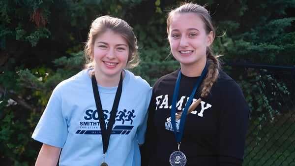 Zwei Schülerinnen der Smithtown Christian School stehen lachend zusammen in einer grünen Außenanlage.