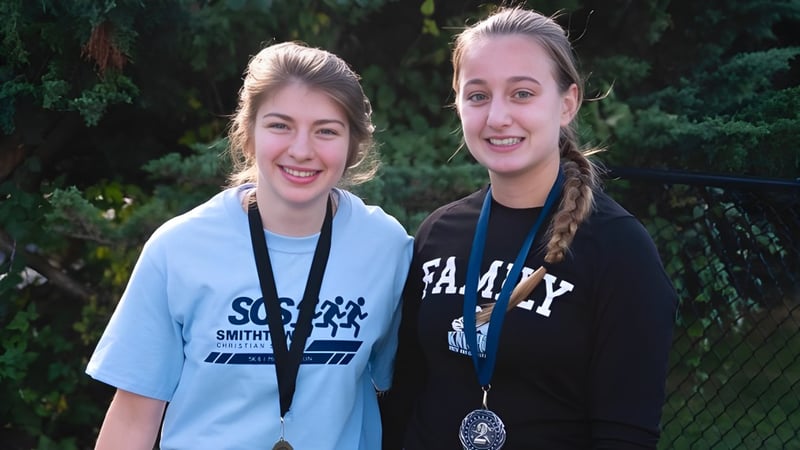 Zwei Schülerinnen der Smithtown Christian School stehen lachend zusammen in einer grünen Außenanlage.