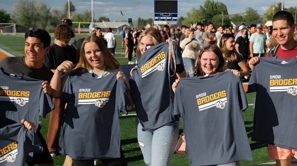 Eine Gruppe Schülerinnen und Schüler mit Snow College Shirts versammelt sich auf dem Sportfeld vor Zuschauern.
