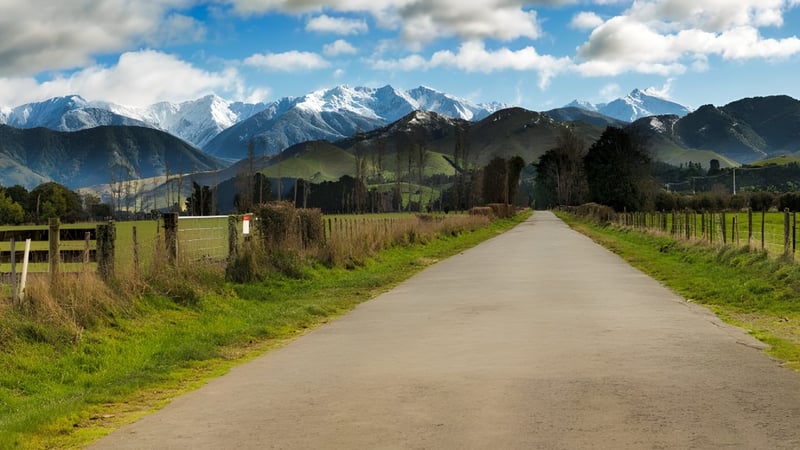 Ein gewundener Feldweg führt durch eine grüne Wiese zu den schneebedeckten Bergen nahe dem Campus des Solway College.
