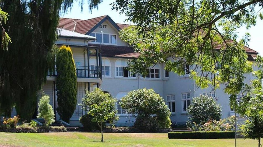 Das Solway College zeigt ein grosses mehrstöckiges Gebäude mit rotem Ziegeldach, umgeben von grüner Bepflanzung.