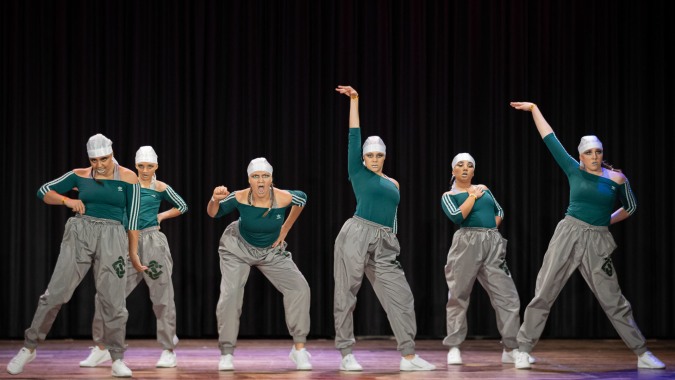 Eine Gruppe von Tänzern in grünen Oberteilen und grauen Hosen tritt auf der Bühne des Solway College auf.