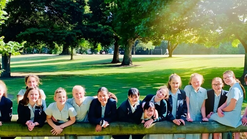 Eine Gruppe Schülerinnen des Solway College sitzt auf einer Wiese umgeben von Bäumen bei sonnigem Wetter.