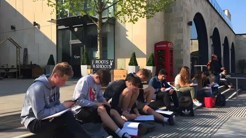 Eine Gruppe junger Menschen sitzt auf dem Bürgersteig vor einem Gebäude auf dem Campus der Somerset Studio School.