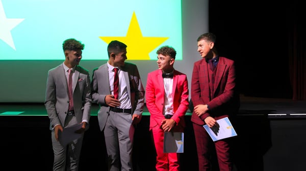 Vier Personen in formeller Kleidung stehen vor einer Kulisse mit einem großen gelben Stern auf dem Campus der Somerset Studio School.