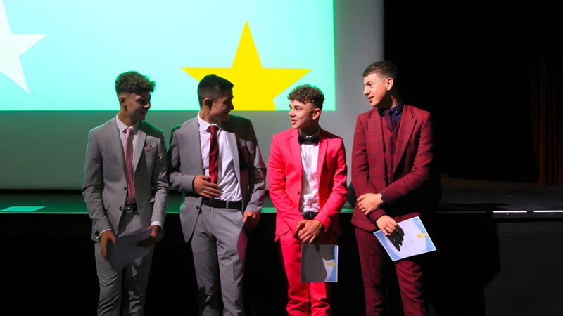 Vier Personen in formeller Kleidung stehen vor einer Kulisse mit einem großen gelben Stern auf dem Campus der Somerset Studio School.