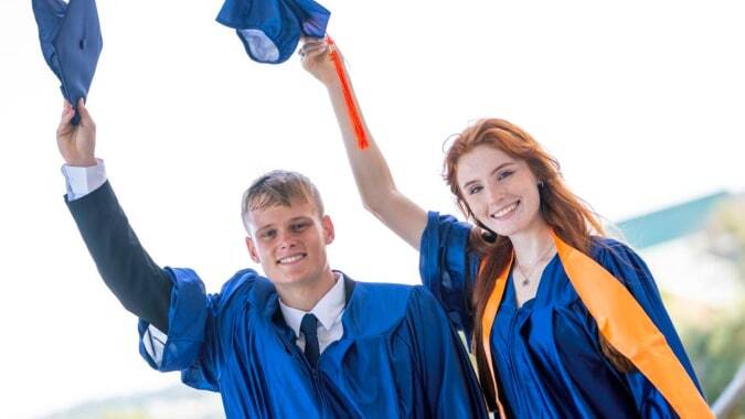 Zwei Absolventen in blauen und orangen Roben feiern ihren Abschluss an der Sotogrande International School im Freien.