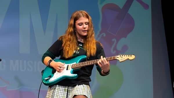 Eine Schülerin der Sotogrande International School spielt E-Gitarre auf einer Bühne mit bunten abstrakten Grafiken im Hintergrund.