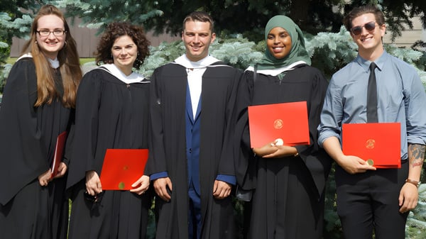 Fünf Personen in akademischer Kleidung stehen auf dem Campus der South Carleton High School vor Bäumen und Grünflächen.