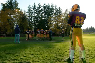 Eine Gruppe von Footballspielern steht auf dem Rasenfeld der South Delta Secondary School vor Bäumen im Hintergrund.