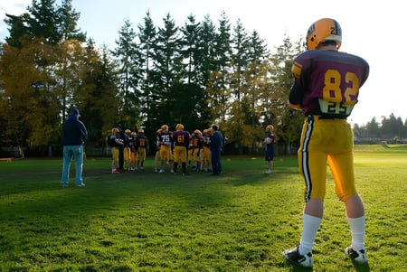 Eine Gruppe von Footballspielern steht auf dem Rasenfeld der South Delta Secondary School vor Bäumen im Hintergrund.