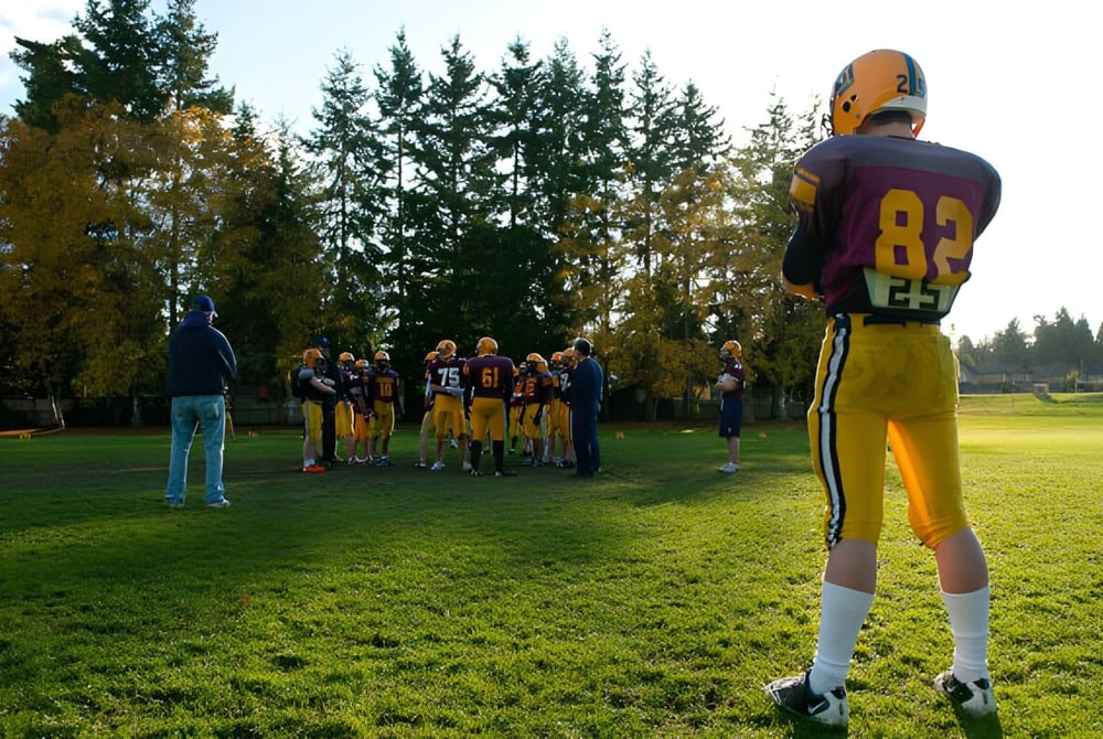 Eine Gruppe von Footballspielern steht auf dem Rasenfeld der South Delta Secondary School vor Bäumen im Hintergrund.