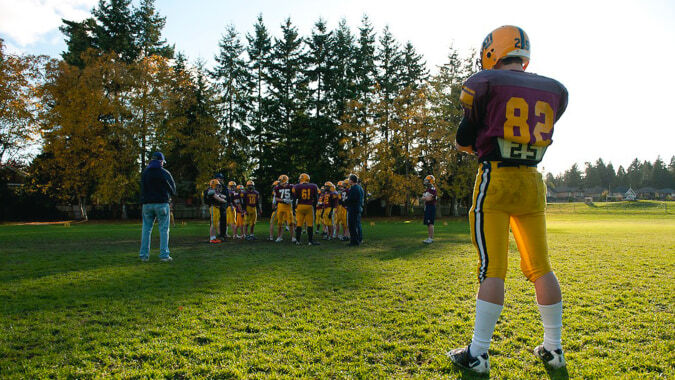 Schüler der South Delta Secondary School stehen in Fußballuniformen auf einem Grasfeld unter bewölktem Himmel.