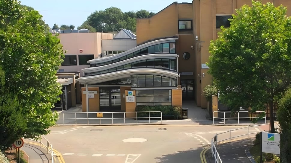 Das moderne Gebäude des South Downs College ist von grünen Bäumen umgeben und durch einen gepflasterten Weg erreichbar.