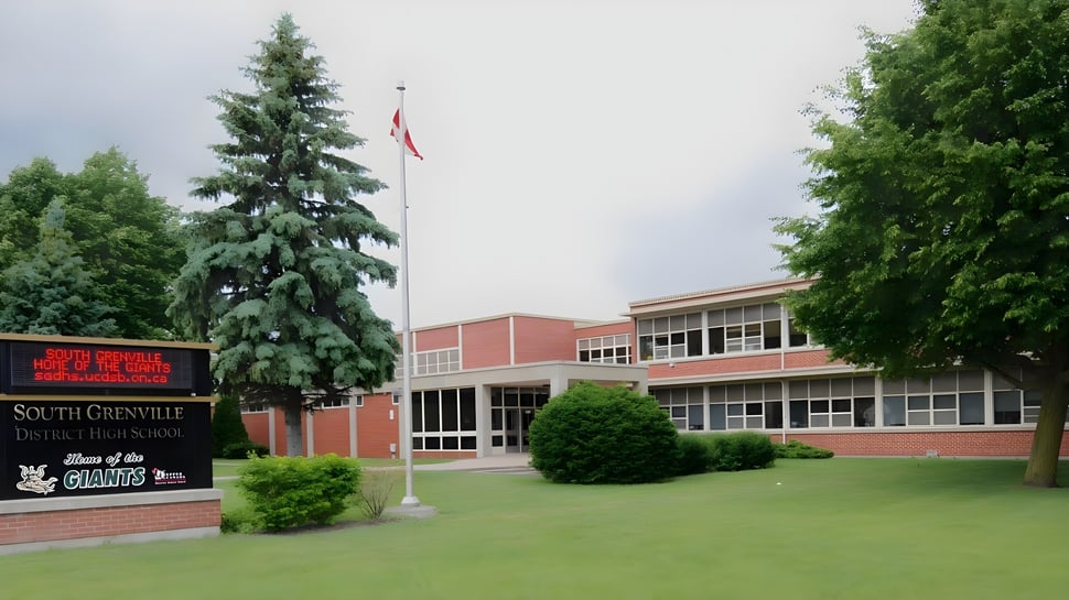 Das Backsteingebäude der South Grenville District High School mit einer kanadischen Flagge und umgeben von Bäumen und Rasen.