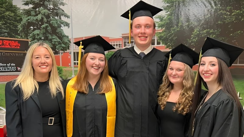 Eine Gruppe von fünf Absolventen steht vor dem Gebäude der South Grenville District High School und feiert ihren Abschluss.