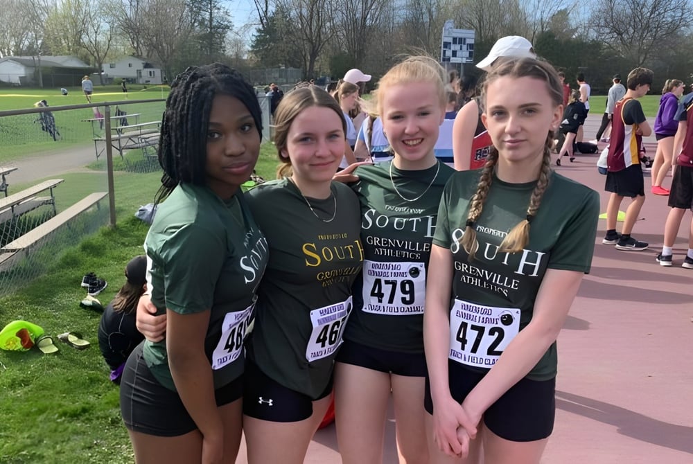 Gruppe von Schülerinnen der South Grenville District High School in grünen und gelben Uniformen steht im Außenbereich auf einem gepflasterten Weg.