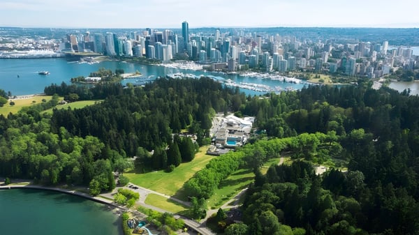 Eine weitläufige Stadtlandschaft mit modernen Wolkenkratzern ist vor einem bewaldeten Gebiet zu sehen.