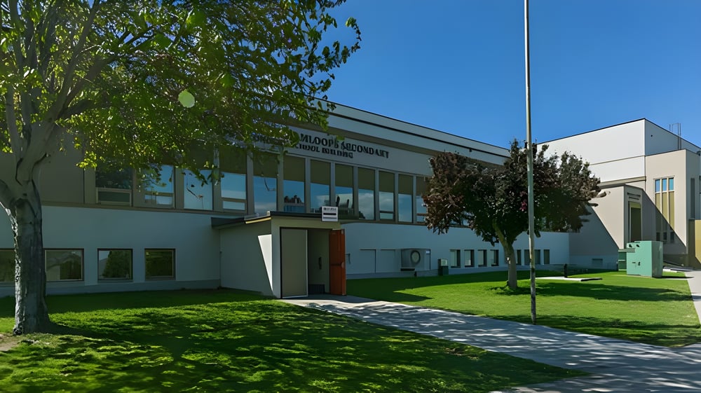Das moderne mehrstöckige Gebäude der South Kamloops Secondary School ist von grüner Vegetation umgeben und hat große Fenster.