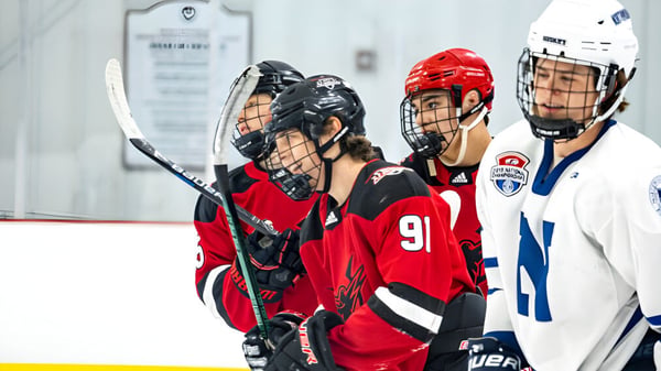 Eine Gruppe von Hockeyspielern in roten und blauen Trikots steht auf der Eisbahn der South Kent School.