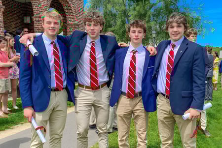 Eine Gruppe Schüler in blauen Anzügen und roten Krawatten steht vor einem Backsteingebäude auf dem Campus der South Kent School.