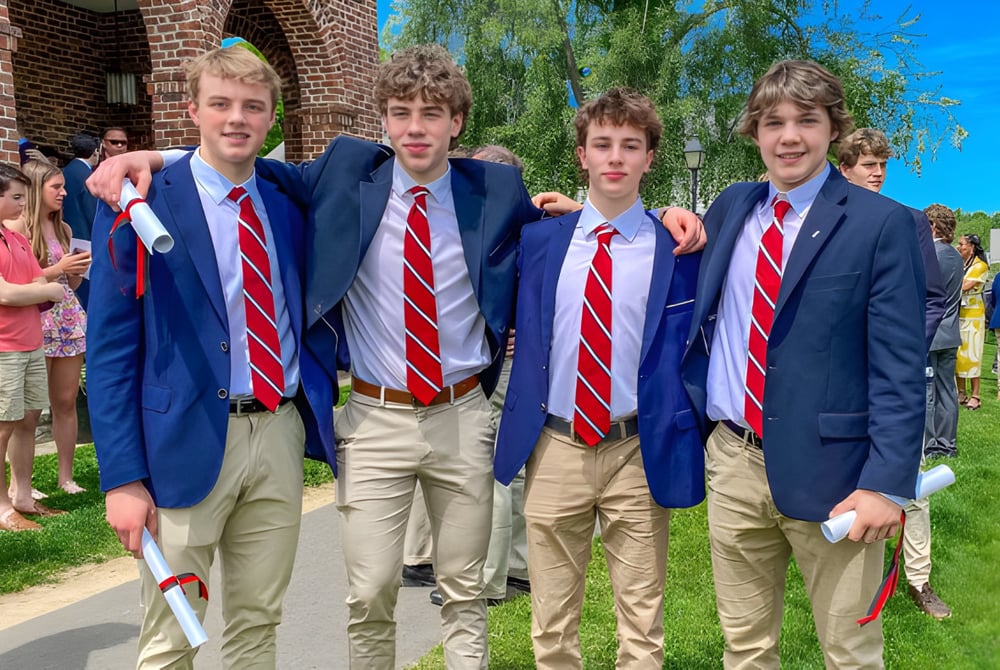 Eine Gruppe Schüler in blauen Anzügen und roten Krawatten steht vor einem Backsteingebäude auf dem Campus der South Kent School.