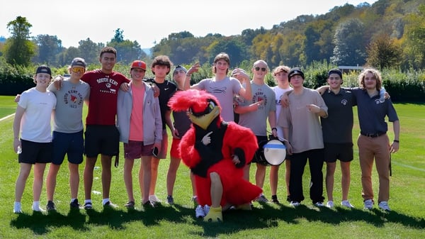 Eine Gruppe von Schülerinnen und Schülern steht auf dem Sportplatz der South Kent School vor einem bewaldeten Hintergrund.