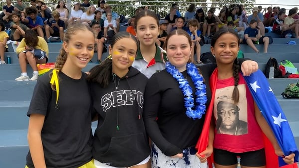 Eine Gruppe junger Schülerinnen posiert gemeinsam auf dem Gelände der South Sydney High School mit einer größeren Menschenmenge im Hintergrund.