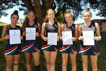 Eine Gruppe junger Sportlerinnen hält vor einem Wald bei der South Sydney High School Zertifikate in der Hand.