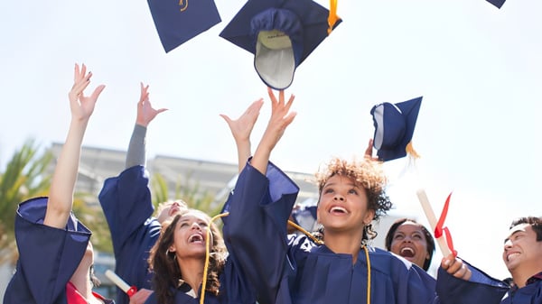 Eine Gruppe von Absolventen der Southport State High School wirft bei einer Feier im Freien ihre blaue Abschlussmütze in die Luft.