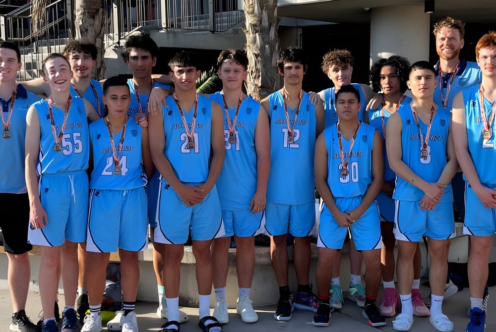 Eine Gruppe Jugendlicher im blauen Basketball-Uniform steht vor dem Gebäude der Southport State High School.