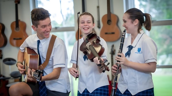 Drei Schüler der Southport State High School spielen Gitarren in einem Raum mit an den Wänden hängenden Gitarren.