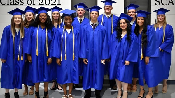 Eine Gruppe von Absolventinnen und Absolventen der Southwest Christian Academy posiert in blauen Talaren vor einer Wand mit der Aufschrift Class of 2021.