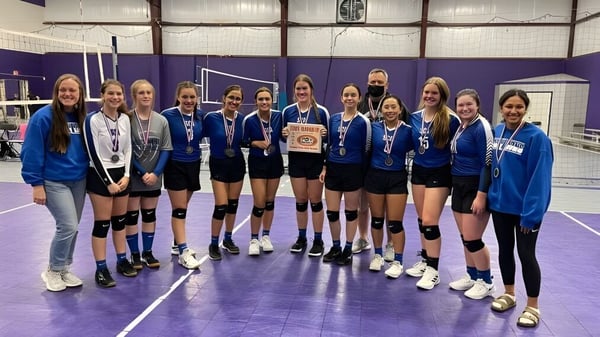 Eine Gruppe junger Volleyballspielerinnen der Southwest Christian Academy hält in der Turnhalle gemeinsam einen Pokal.