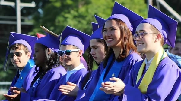Eine Gruppe von Absolventinnen und Absolventen in violetten Talaren feiert ihren Abschluss auf dem Gelände der Sparhawk School.