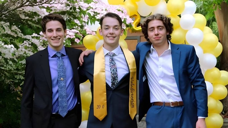 Drei Schüler in formeller Kleidung stehen vor blühenden Bäumen und gelben Luftballons auf dem Gelände der Spectrum Community Secondary School.