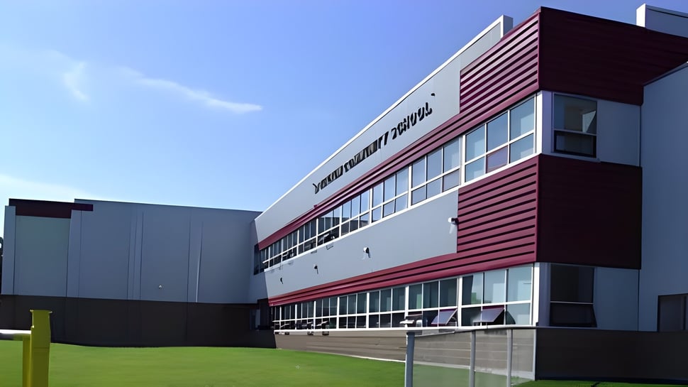 Das moderne mehrstöckige Gebäude der Spectrum Community Secondary School mit roter und weißer Fassade steht umgeben von einer grünen Wiese.