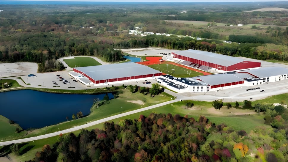 Der landwirtschaftliche Komplex der SPIRE Academy mit roten Dächern liegt eingebettet in eine bewaldete Landschaft neben einem Teich.