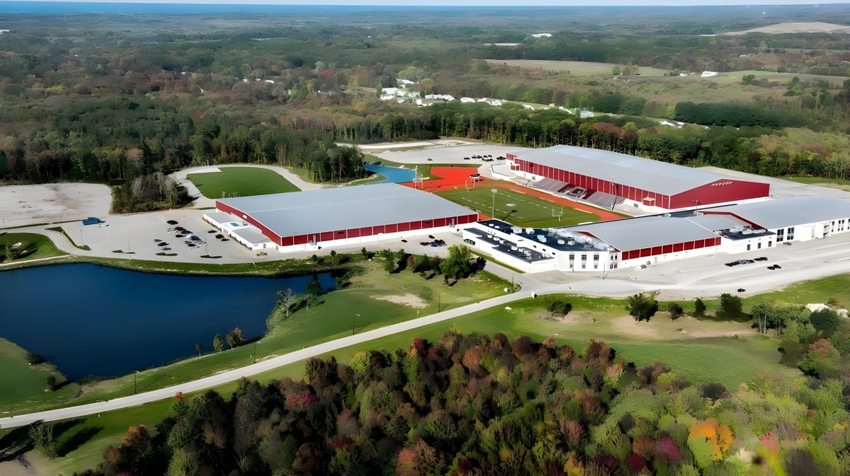 Der landwirtschaftliche Komplex der SPIRE Academy mit roten Dächern liegt eingebettet in eine bewaldete Landschaft neben einem Teich.