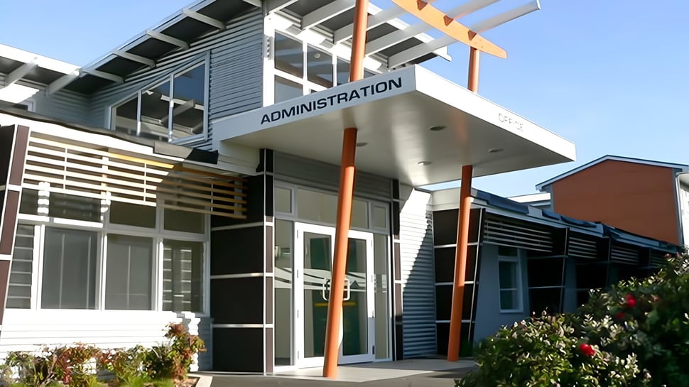 Das moderne Verwaltungsgebäude mit einem deutlich sichtbaren Schild der Spotswood College ist von grüner Vegetation umgeben.